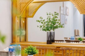 A room with a wooden bench, a small potted plant, and a mirror reflecting a plant and a wall with framed pictures. - VietHOME - 22 Pho Hue - Duplex 3 4 (Hanoi)