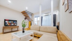 A modern living room with a sectional sofa, a glass coffee table, and a TV on a wooden stand. - VietHOME - 22 Pho Hue - Duplex 3 4 (Hanoi)