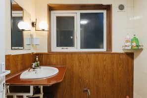 A bathroom with a wooden vanity, a white sink, and a window above the mirror. - VietHOME - 22 Pho Hue - Duplex 3 4 (Hanoi)