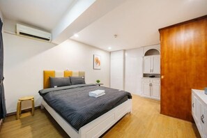 A bedroom with a bed, bedside table, and a small stool. There is a wooden wardrobe and a white cabinet in the room. - VietHOME - 22 Pho Hue - Duplex 3 4 (Hanoi)