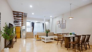 A spacious living area with a sofa, coffee table, dining table with chairs, and a staircase leading to another room. - VietHOME - 22 Pho Hue - Duplex 3 4 (Hanoi)