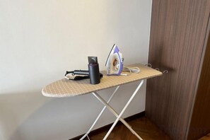 A corner of a room with a wooden door, a wall, and an ironing board with an iron, a mug, and a hairdryer. - Landmark by Homey Planet 3BR Family Suite(B) (Tanjung Tokong)