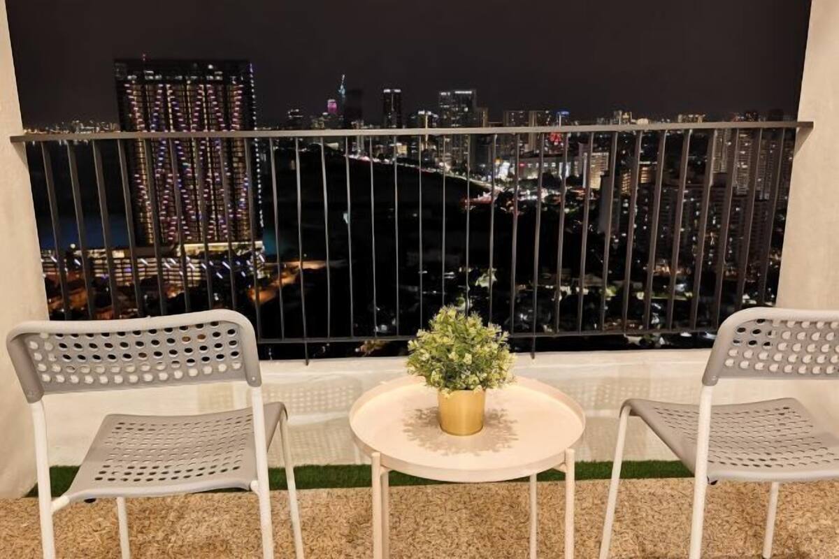 A balcony with two chairs and a small table, featuring a cityscape view at night.