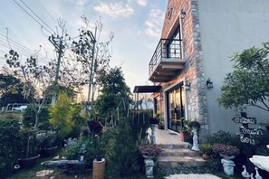 A building with a stone facade, a balcony, and a garden with various plants and a pathway leading to the entrance. - Baanjeab in khaoyai (Pak Chong)