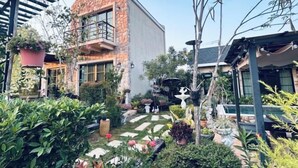 A modern house with a stone facade, a balcony, and a garden with various plants and a pathway. - Baanjeab in khaoyai (Pak Chong)