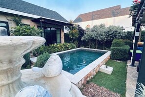 A swimming pool with a stone border, surrounded by a well-maintained lawn and various plants. - Baanjeab in khaoyai (Pak Chong)