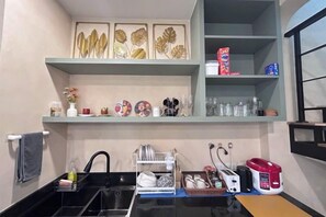 A kitchen with a black countertop, a sink, and a dish rack. There are shelves above the counter with decorative items and kitchenware. - Baanjeab in khaoyai (Pak Chong)