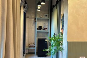 A narrow hallway with a black refrigerator, a shelf with a kettle, and a potted plant. - Baanjeab in khaoyai (Pak Chong)