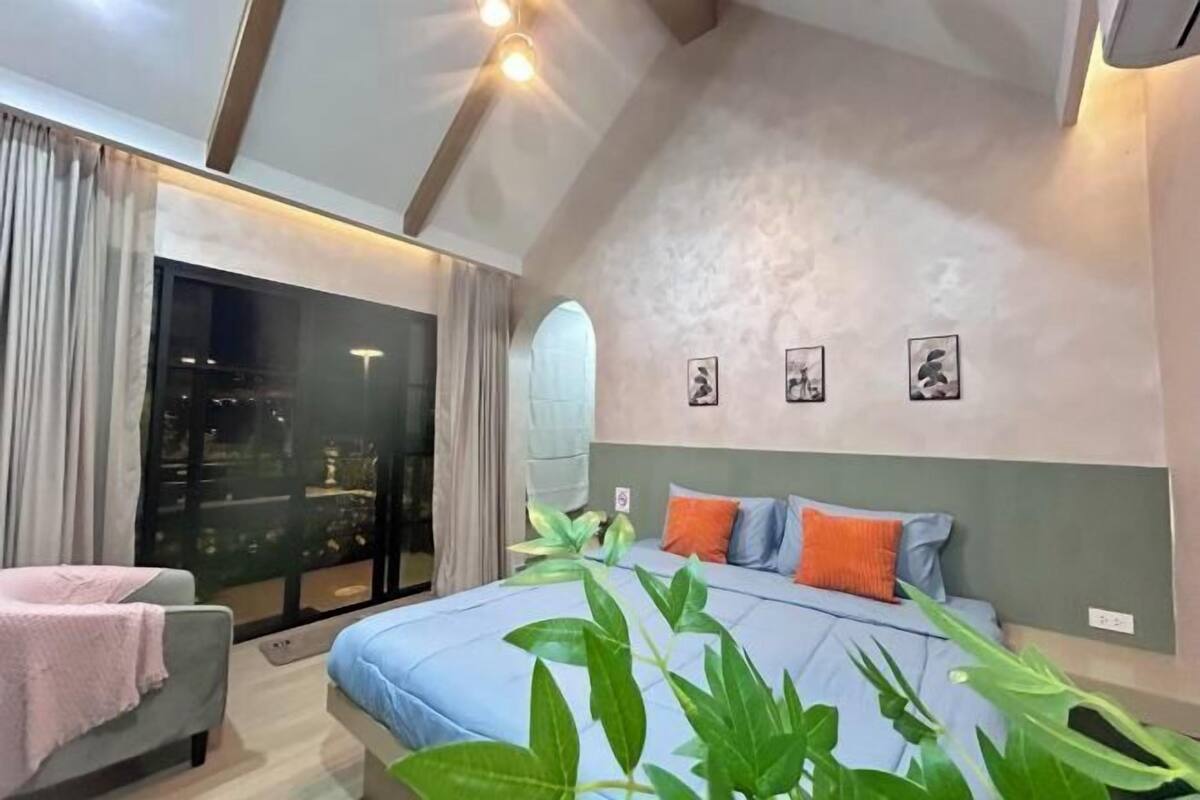 A bedroom with a bed, a window, a plant, and a wall with three pictures.