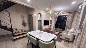 A modern living room with a dining area, a staircase, and a TV mounted on the wall. - Baanjeab in khaoyai (Pak Chong)