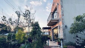 A building with a stone facade, a balcony, and a garden with various plants and a pathway leading to the entrance. - Baanjeab in khaoyai (Pak Chong)