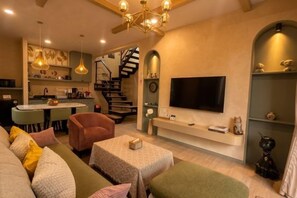 A modern living room with a sofa, coffee table, and a TV mounted on the wall. A staircase leads to an upper level. - Baanjeab in khaoyai (Pak Chong)