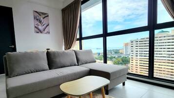 A modern living room with a grey sofa, a wooden coffee table, and a large window with a city view.