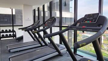 Un gimnasio con cintas de correr y mancuernas, ventanas amplias y vistas de la ciudad.
