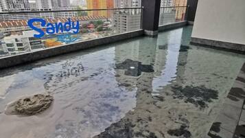 A wet floor with a puddle and a sandy area, a glass railing, and a view of buildings in the background.