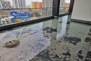 A wet floor with a puddle and a sandy area, a glass railing, and a view of buildings in the background. - Urban Muji Retreat Suites (George Town)