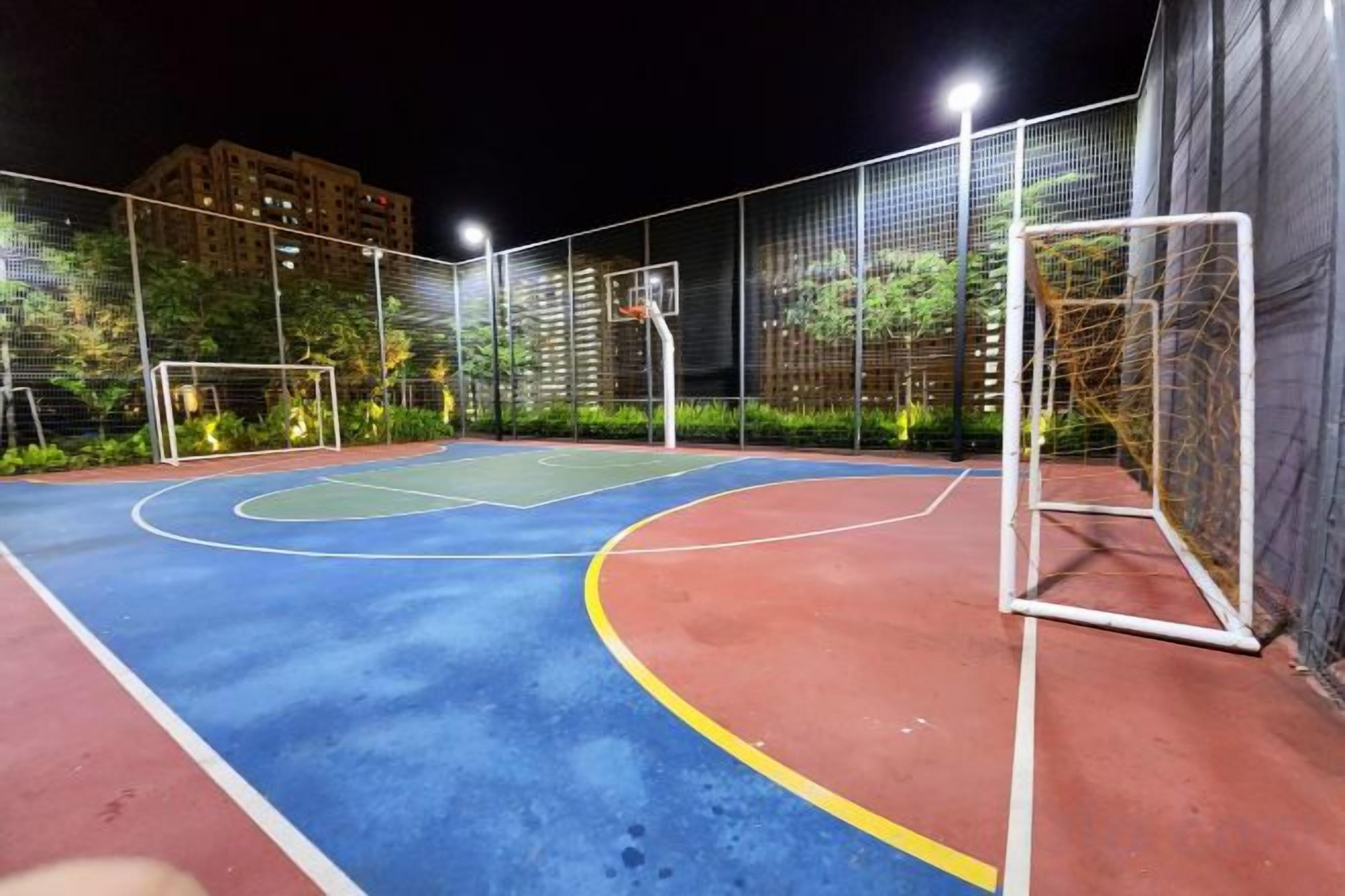 An outdoor basketball court at night with a goal post and a fence.