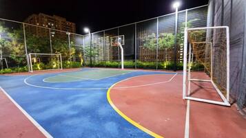 An outdoor basketball court at night with a goal post and a fence.
