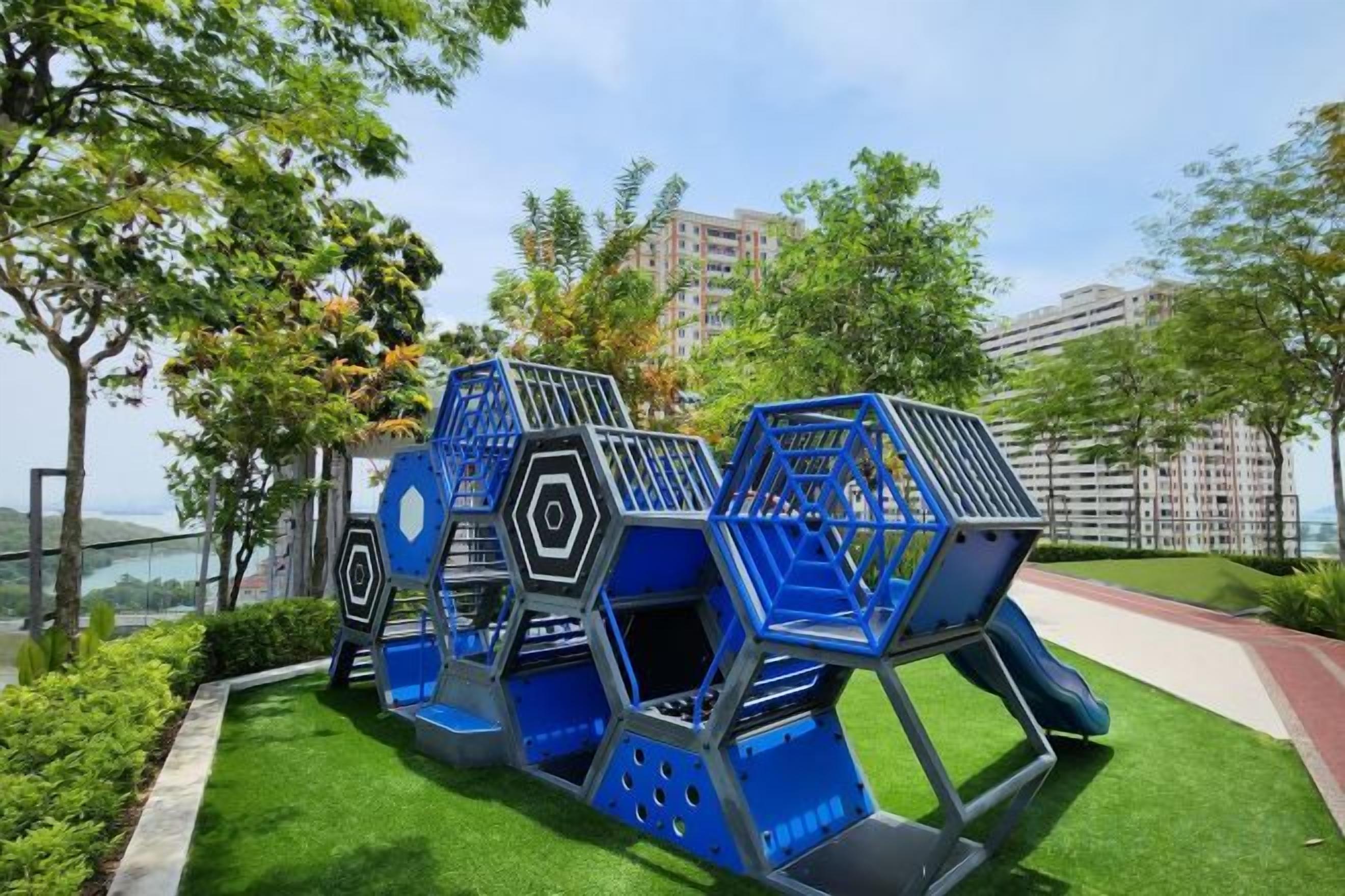 A playground with blue and gray play structures, surrounded by green grass and trees.