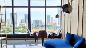 A modern living room with a large window, a blue sofa, a round coffee table, and two chairs. - Urban Muji Retreat Suites (George Town)