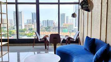 Una sala de estar moderna con un sofá azul, una mesa de centro redonda y vistas a la ciudad a través de amplias ventanas.