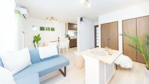 Una sala de estar moderna con un sofá azul, una pequeña mesa de comedor y una cocina al fondo.