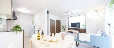 A modern living space with a dining area, a sofa, a TV, and a kitchen area.
