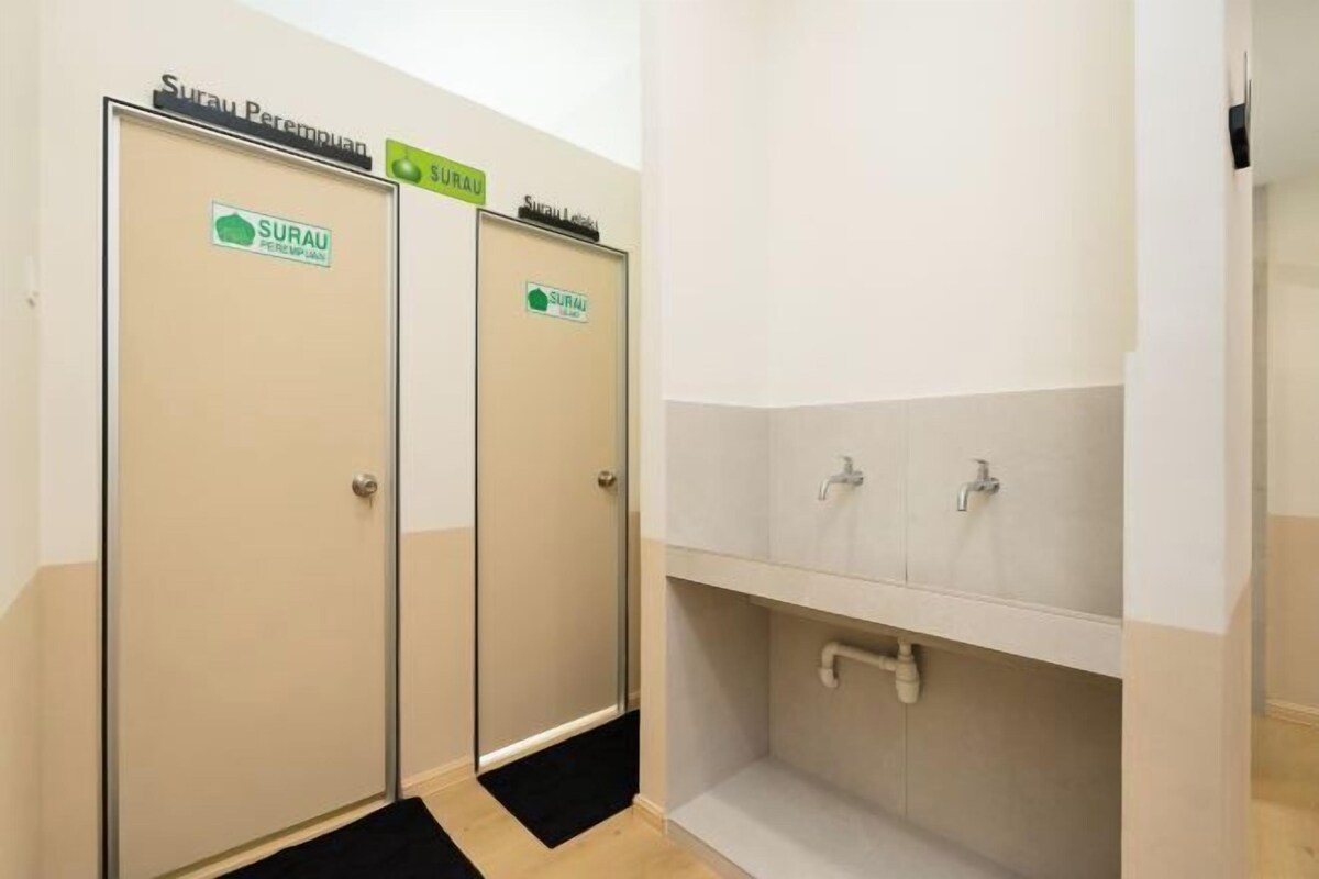 A restroom with two doors labeled 'SURAU' and a sink area with a mirror and faucets.