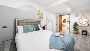 Quarto moderno com uma cama grande, mesa de cabeceira, espelho e uma pequena planta.