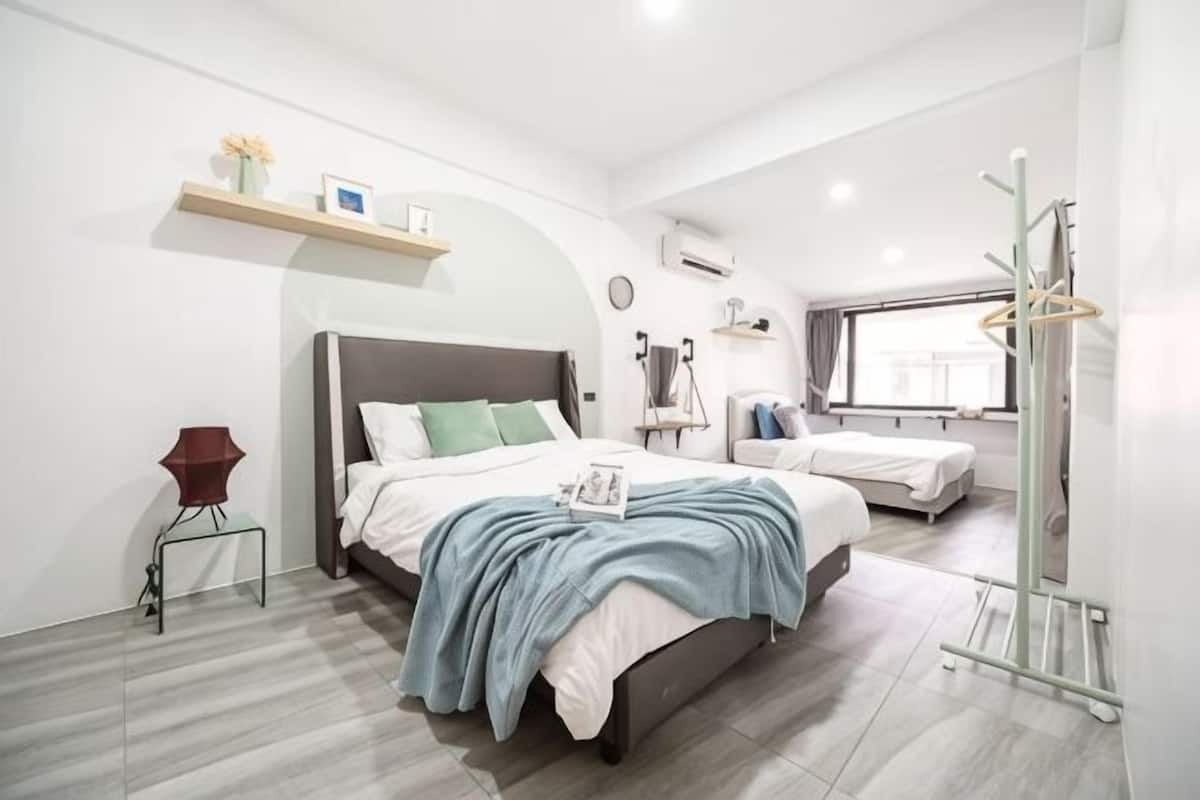 Une chambre d’hôtel moderne dotée d’un grand lit, d’un plus petit lit, d’une coiffeuse avec un miroir, d’un porte-manteau et d’une fenêtre offrant une vue.