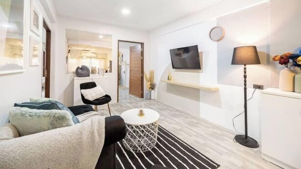 Uma sala de estar moderna com um sofá, uma mesa de centro redonda, uma TV, um abajur e uma pequena mesa lateral.