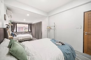 Een hotelkamer met een bed, nachtkastje, raam met gordijnen, kledingkast en een deur.