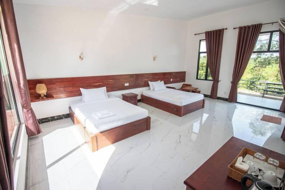 A hotel room with two beds, a wooden headboard, a marble floor, and large windows with curtains.