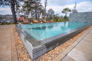 Une piscine rectangulaire bordée de pierres, entourée d’un chemin de galets et agrémentée de chaises longues et de parasols.
