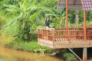 Une terrasse en bois s’étendant au-dessus d’une étendue d’eau, entourée d’une végétation luxuriante et de bananiers.