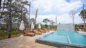 A swimming pool with lounge chairs and umbrellas, surrounded by trees and a stone wall.