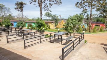 An outdoor seating area with tables and benches, surrounded by trees and buildings with colorful facades.