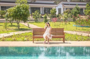 Una persona sentada en un banco junto a una piscina, con un edificio al fondo.