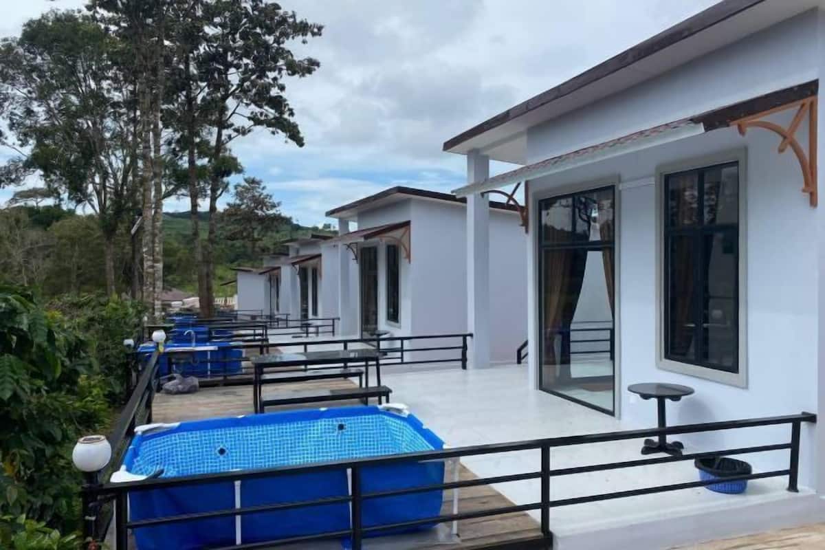 A row of white buildings with large windows, a blue pool, and outdoor seating.