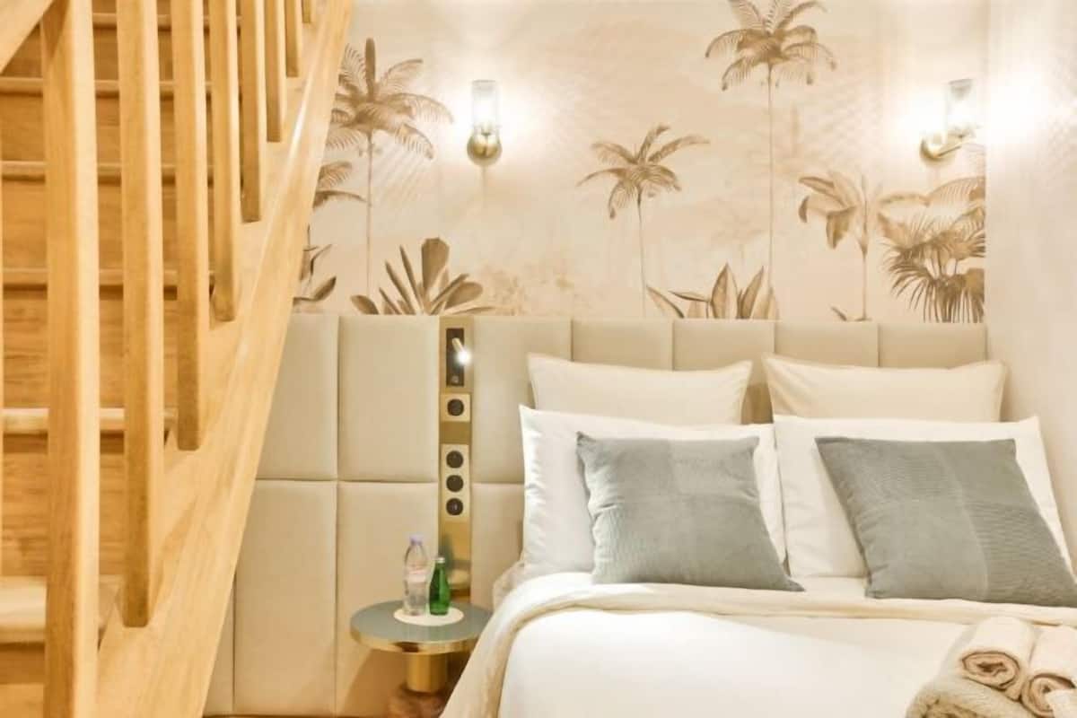 A hotel room with a bed, a nightstand, and a wall with palm tree wallpaper.