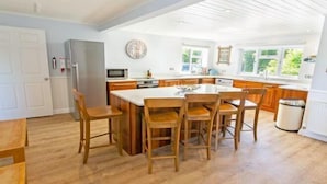 Une cuisine spacieuse avec des meubles en bois, un grand îlot central doté de tabourets de bar et une vue sur l’extérieur grâce aux fenêtres.