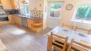 A compact kitchen with wooden cabinets, a built-in microwave, and a dining area with a table set for four. - Cloudbreak Hot Tub Log Burner, Dogs Welcome (Heanton Punchardon)