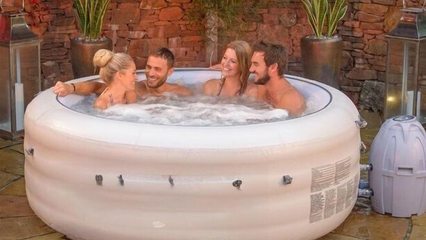 A hot tub with four people, surrounded by potted plants and a stone wall. - Cloudbreak Hot Tub Log Burner, Dogs Welcome (Heanton Punchardon)