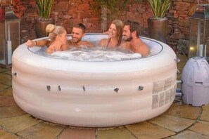 A hot tub with four people, surrounded by potted plants and a stone wall. - Cloudbreak Hot Tub Log Burner, Dogs Welcome (Heanton Punchardon)