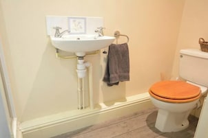 Un baño con un lavamanos blanco, un asiento de váter de madera y una toalla colgada en un perchero.