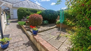 A garden pathway leading to a house with a covered porch, surrounded by various plants and a green umbrella. - Cloudbreak Hot Tub Log Burner, Dogs Welcome (Heanton Punchardon)