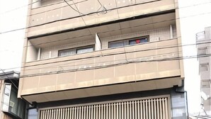 A multi-story building with a beige facade, multiple balconies, and a large, closed metal shutter at the ground level. - Guest houseNear Nijo CastleNear and quiet from the station A185 (Kyoto)