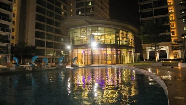 A nighttime view of a hotel with a circular pool reflecting lights, surrounded by high-rise buildings.