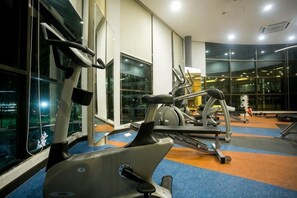Un gimnasio con equipo de ejercicio, ventanas amplias y alfombra azul.