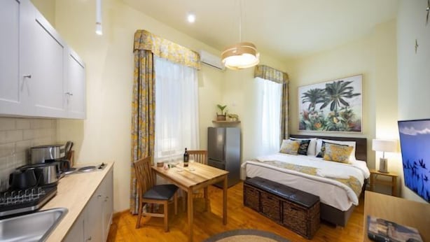 A compact hotel room with a kitchenette, a bed with a headboard, a dining table, and a large window with curtains. - Rainforest Studio Downtown by Pretty Apartments (Bucharest)